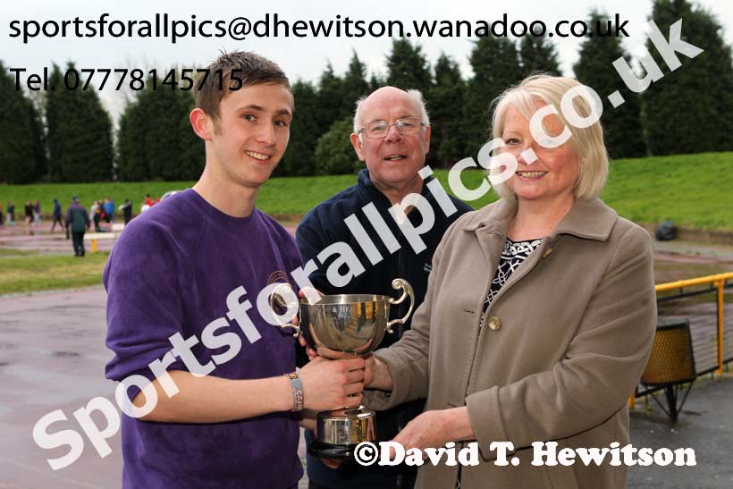 Michael Wilson (Sunderland) receives the Jimmy Hedley 800 metres Cup from Diane Holmes, daughter of the late Jimmy Hedley and Chris Betts, North Eastern Grand Prix, Monkton Stadium, Jarrow. Photo: David T. Hewitson/Sports for All Pics